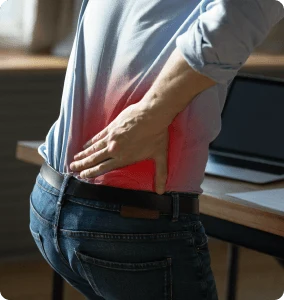 A man stands in front of a laptop, holding his back in pain